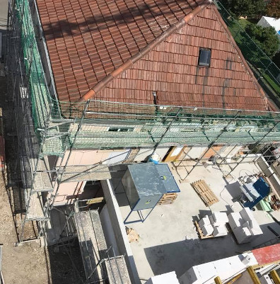 Dacharbeiten an einem Haus mit rotem Ziegeldach und Baugerüsten.